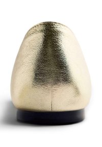 Chaussure plate en métal doré avec une texture en cuir lisse, bout arrondi et semelle en caoutchouc noir. Design simple sans embellissements.