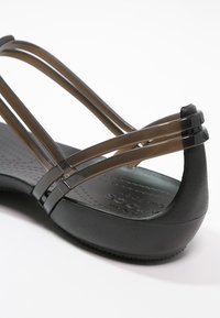 Sandale compensée noire avec doubles brides marron transparentes croisant le talon et semelle perforée pour le confort.