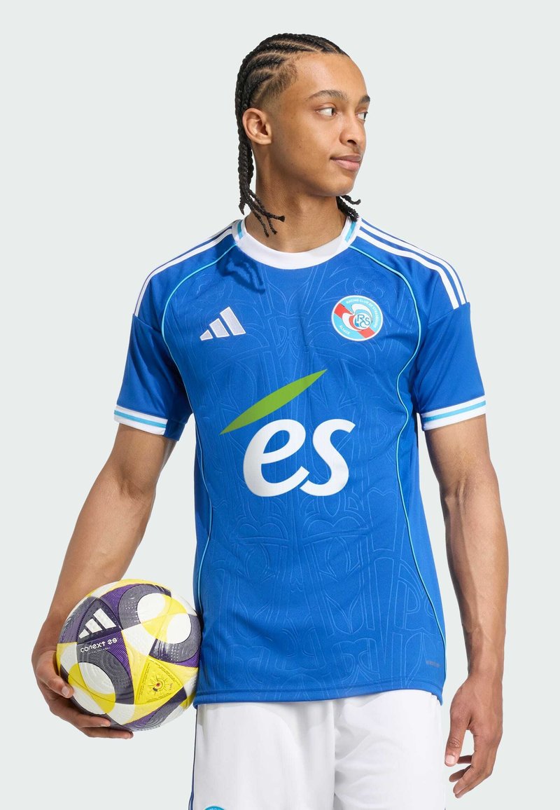 Blaues Fußballtrikot mit kurzen Ärmeln und weißen Akzenten, das über eine erhabene Textur und ein großes "es"-Logo verfügt. Das Modell hält einen gemusterten Fußball.