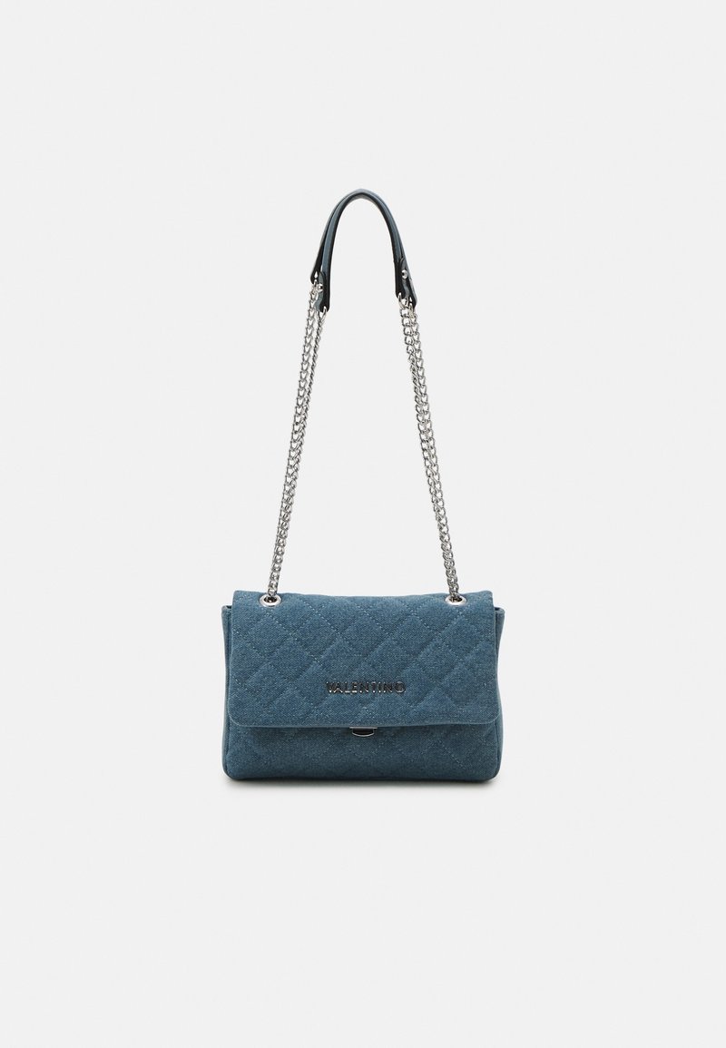 Quiltad blå tyghandväska med en silverkedjeslunga, med en framflik och en inlägg med logotyp. Slät yta och strukturerad form.