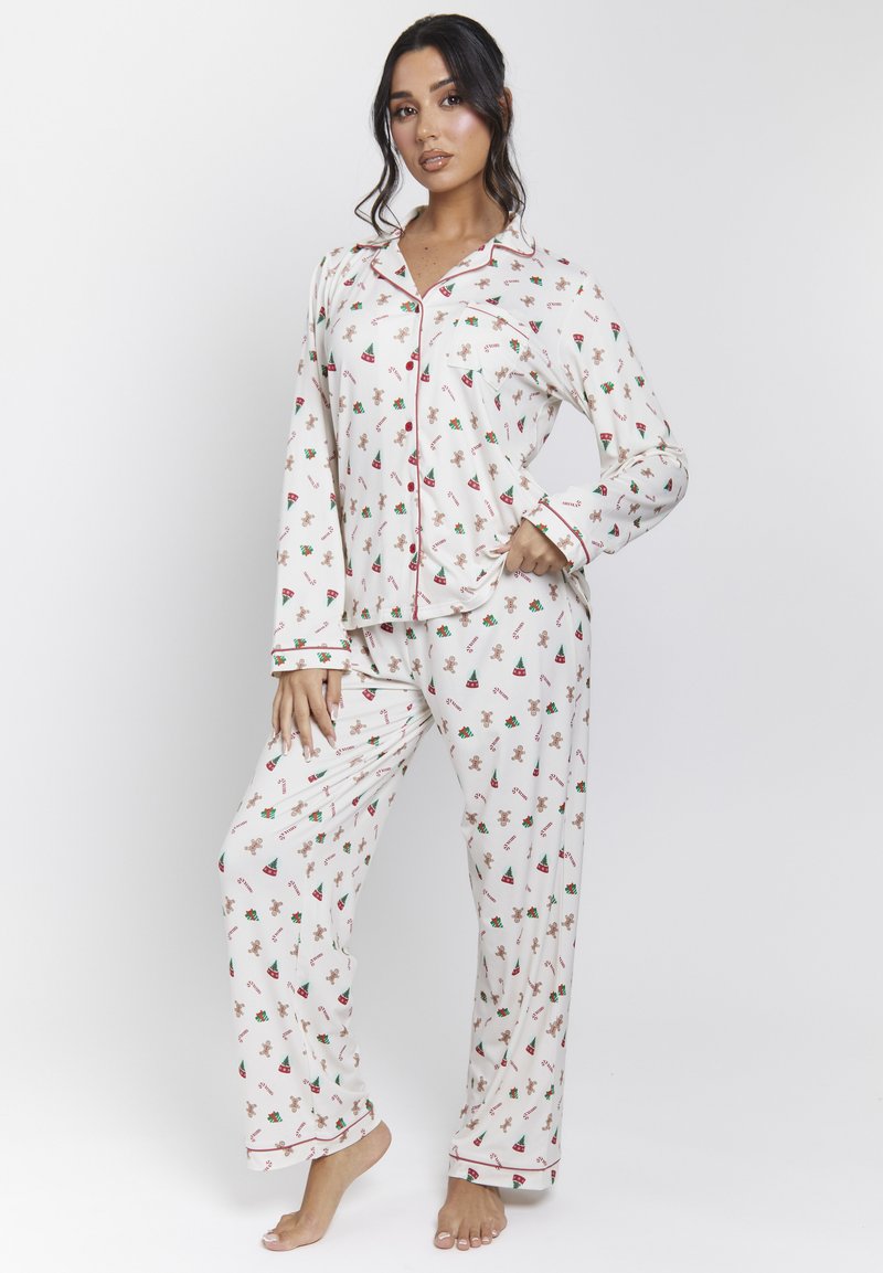 Witte pyjama-set met rode accenten, voorzien van een speels patroon van peperkoekmannen en kerstbomen. Lange mouwen en losse broek.