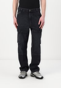 Svart cargo-bukser med flere lommer, en avslappet passform, og stoff med strukturert denim. Brukt med sølvfargede joggesko.