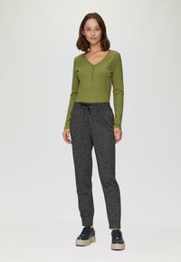 Grüner gerippter Strickpullover mit langen Ärmeln, V-Ausschnitt und Knöpfen, kombiniert mit strukturierten grauen Jogginghosen und schwarzen Plateau-Sneakern.