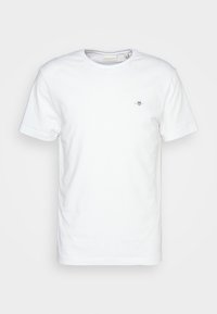 Weißes T-Shirt mit kurzen Ärmeln und Rundhalsausschnitt, mit kleinem gesticktem Logo auf der linken Brust und einem Markenetikett im Kragen.