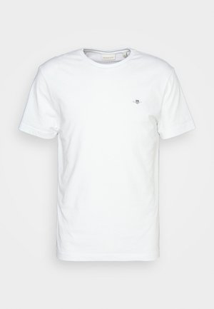 T-shirt en coton blanc avec un col rond et des manches courtes, arborant un petit logo sur la poitrine et une texture lisse et propre.