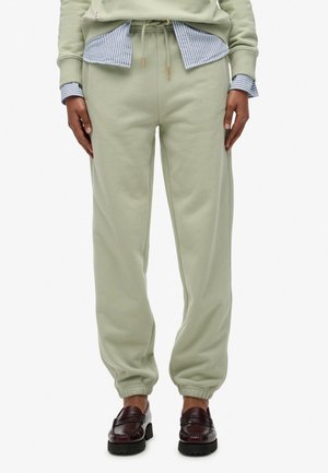 Pantalons de survêtement vert clair en matériau doux, avec une taille élastique munie d'un cordon de serrage et des ourlets resserrés. Associés à une chemise rayée bleu en dessous.