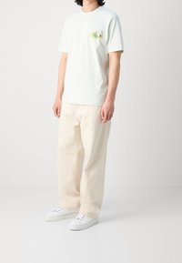 Ljusgrön bomullst-shirt med en bröstgrafik, tillsammans med löst sittande krämfärgade byxor och vita sneakers. Enkel rundad halsringning.