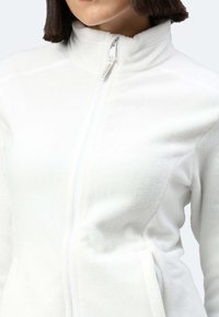 Giacca in pile bianca con zip, dotata di un colletto alto, con una texture liscia e tasche laterali, accentuata da un tassello della zip.