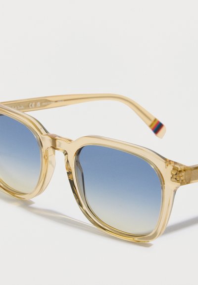 Priehľadné svetložlté slnečné okuliare so štvorcovými sklami, s modrým gradientným tónovaním a jemným viacfarebným akcentom na stráne.