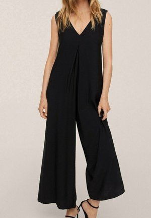 Combinaison noire sans manches avec un décolleté en V, un devant plissé, un design à jambes larges et une texture lisse, assortie à des brides de cheville noires.