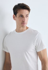 T-shirt en coton blanc avec un col rond et des manches courtes, offrant une texture lisse et un design simple, porté par un mannequin masculin sur un fond clair.