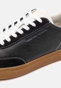Sneakers en cuir noir et blanc avec lacets blancs, semelle en caoutchouc naturel, et embossage discret "CLAE LOS ANGELES" sur le côté.