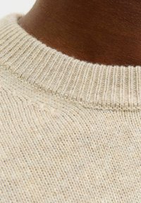 Licht beige gebreide trui met een geribbelde kraagstructuur. Close-up van de kraag, die de zachte vezels en subtiele kleurnuances laat zien.