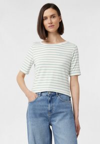 Pasekowaną koszulka z krótkim rękawem w kolorze białym i jasnoniebieskim, z okrągłym dekoltem i przeszyciem na klatce piersiowej. Połączona z jasnoniebieskimi dżinsami.