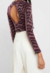 Långärmad topp med ett rikt mönster i burgundy och rosa, med en skuren rygg och scallopade ärmslut, tillverkad av texturerad tyg.