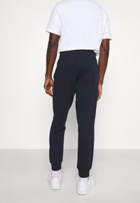 Dunkelblaue Sweatpants aus weichem Stoff mit schmal zulaufendem Design, elastischem Bund und einer Gesäßtasche. Kombiniert mit weißen Sneakers.