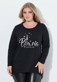 Schwarzes Langarmshirt mit weißem Grafikdruck des Eiffelturms und dem Text "Paris" sowie rosa Herzen. Weicher Stoff, lässige Passform, abgerundeter Saum.