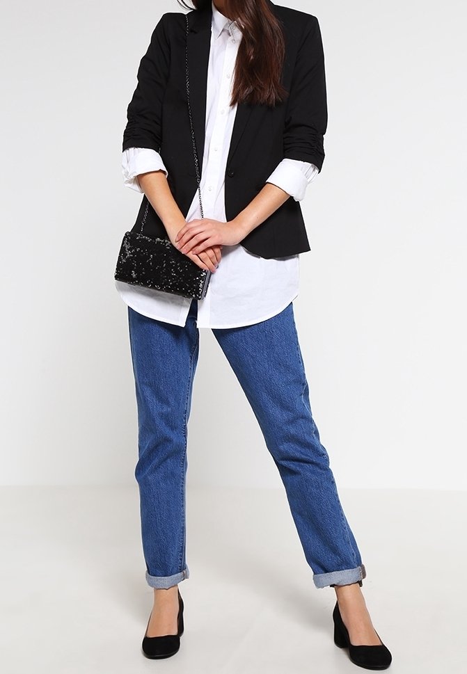Svart blazer över en vit skjorta, kombinerad med uppvikt blå jeans och svarta spetsiga klackar. Liten svart handväska med texturerad yta.