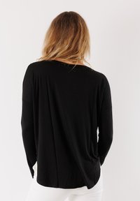 Top nero a maniche lunghe con un fit rilassato, texture morbida e scollatura a barco. Presenta spalle cadute e spacchi laterali per facilitare i movimenti.