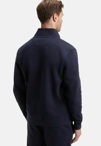 Sweat-shirt bleu marine avec un tissu texturé, un col montant et des poignets et un ourlet côtelés. La vue arrière montre un détail de couture minimal.