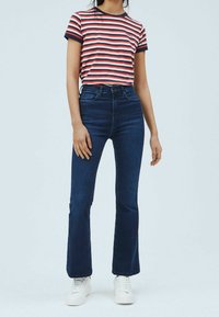 Stribet t-shirt i rød, hvid og marineblå; højttaljede mørkeblå buks med flared ben; hvide sneakers; afslappet outfit med minimal udsmykning.
