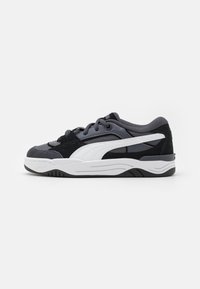 Chaussures de sport noires et grises en matériaux suédé et mesh, avec une rayure latérale blanche, un col rembourré et une épaisse semelle en caoutchouc blanche.