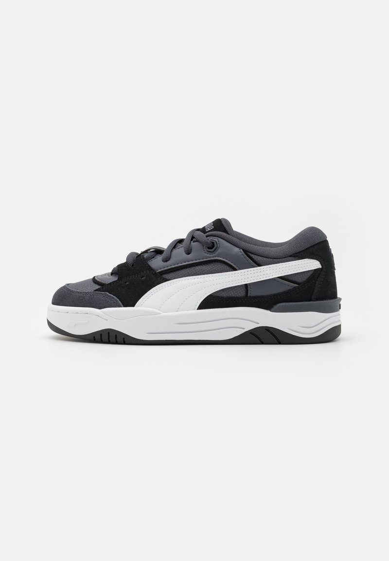 Chaussures de sport noires et grises en matériaux suédé et mesh, avec une rayure latérale blanche, un col rembourré et une épaisse semelle en caoutchouc blanche.