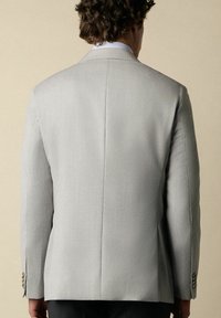 Veste de costume gris clair au fit ajusté, avec une texture lisse, des manches longues et des poignets boutonnés. La vue arrière montre des lignes épurées.