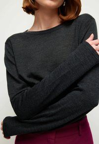 Tummanharmaa pitkähihaisen neuleen neulottu pehmeä kangas, jossa on löysä istuvuus ja leveät kalvosimet. Minimalistinen muotoilu, jossa on pyöreä pääntie.