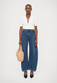 Top bianco a coste con scollo a V e dettaglio in pizzo, jeans in denim blu a vita alta e gamba larga, décolleté neri a punta e una morbida borsa beige.