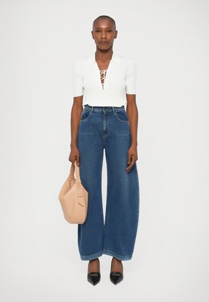 Top bianco a coste con scollo a V e dettaglio in pizzo, jeans in denim blu a vita alta e gamba larga, décolleté neri a punta e una morbida borsa beige.