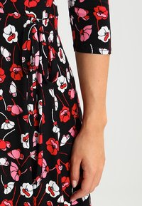 Black dress with red, pink, and white floral print. Features a tie at the waist, three-quarter sleeves, and soft, textured fabric.