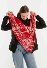 Czerwono-biały, wzorzysty, dzianinowy szal noszony na czarnej koszuli, prezentujący trójkątny kształt z miękką teksturą i frędzlami na brzegach.