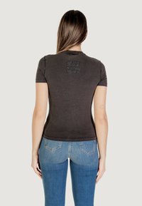 T-shirt grigio scuro a maniche corte con un design aderente e una sottile grafica testurizzata sulla parte superiore della schiena. Abbinato a jeans in denim blu.