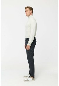 Weißer Rollkragenpullover, dunkelgraue maßgeschneiderte Hose und Sneaker mit weißen, grauen und schwarzen Akzenten. Die Seitenansicht zeigt die Passform und Designdetails.