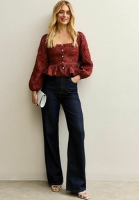 Blusa texturizada de color vino con escote cuadrado y mangas abullonadas, combinada con pantalones de mezclilla oscuros de pierna ancha de cintura alta y sandalias plateadas.