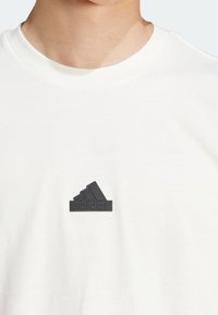 Camiseta de algodón blanca con un logotipo negro de goma de adidas en el pecho, con cuello redondo y mangas cortas.
