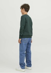Felpa verde scuro con maniche lunghe e polsini a coste, abbinata a jeans dritti azzurri e sneakers bianche.