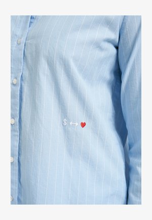 Light blue pinstriped shirt with small embroidered white dollar sign, white double-headed arrow, and red heart near the waist.