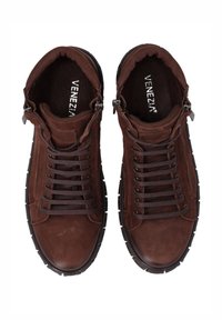 Brązowe skórzane sneakersy na sznurówki charakteryzują się teksturowanym wierzchem, miękką wyściółką oraz gumową podeszwą z kontrastującymi czarnymi akcentami. Nazwa marki widoczna wewnątrz.