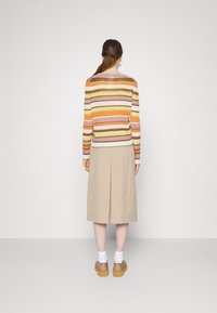 Pull en tricot rayé multicolore à manches longues, associé à une jupe beige longueur genou et des chaussures à plateforme marron. Design simple, coupe décontractée.
