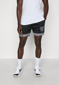 Juodos ir pilkos tinklinės sportinės šortai su spausdintu "Raiders" logotipu kairėje. Yra tekstūruotas dizainas ir šoninės juostelės.