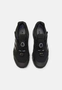 Czarne sneakersy GORE-TEX z siateczkową cholewką, teksturowaną powierzchnią, elastycznymi sznurówkami typu bungee oraz trzema szarymi paskami po bokach.