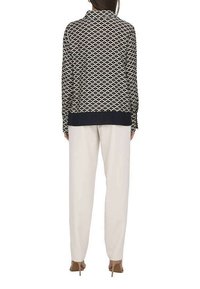 Blouse imprimée en noir et crème avec un motif texturé, dotée d'un col et d'un ourlet bleu marine. Associée à un pantalon clair et des talons.