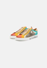 Une paire de baskets basse avec des panneaux orange, jaune, gris et turquoise, des lacets blancs et des semelles blanches, avec un texte noir sur le côté.