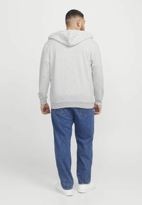 Grå hættetrøje med kengurulomme, ribbede kanter og manchetter. Båret med løstsiddende blå jeans og hvide sneakers.
