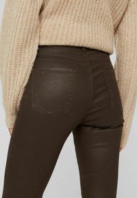 Bruna högmidjade jeans med en åtsittande silhuett, som har två bakfickor och en slät textur, ihop med en beige stickad tröja.