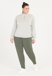 Lys grå lynlås sweatshirt med guld lynlås, parret med olivengrønne tapered joggers og hvide sneakers. Glat stof og afslappet pasform.