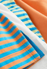 Couches de tissu en coton dans des couleurs orange et blanche, avec des motifs rayés de bleu et orange, présentant une texture lisse et des coutures bien définies.