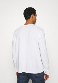 T-shirt bianco a maniche lunghe realizzato in cotone, con scollo a girocollo e vestibilità comoda. Tessuto liscio con dettagli di cucitura minimi.